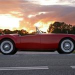 Beautiful red old cabriolet with white tires on the road against a cloudy sky